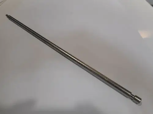 Verstellbare Schraube aus Metall, abgebildet auf einem weißen Hintergrund, mit Remeha-Logo am Ende. Die Schraube hat eine schmale, längliche Form.